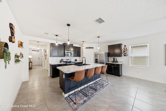 5071 Talbot Blvd, Cocoa, FL 32926 - kitchen with appliances with stainless steel finishes, light tile patterned flooring, an island with sink, a breakfast bar area, and a textured ceiling