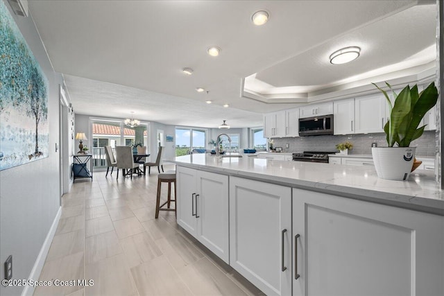 8954 Puerto Del Rio Dr Unit 1503, Cape Canaveral, FL 32920 - kitchen featuring appliances with stainless steel finishes, white cabinets, a chandelier, tasteful backsplash, and light stone counters