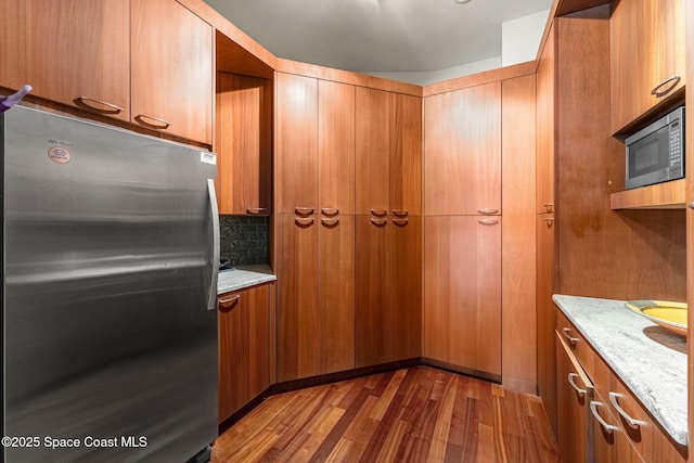 2375 S Atlantic Ave Unit 601, Cocoa Beach, FL 32931 - kitchen with freestanding refrigerator, wood finished floors, brown cabinetry, tasteful backsplash, and light stone counters