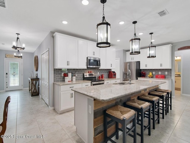 9025 106th Ave, Vero Beach, FL 32967 - kitchen with appliances with stainless steel finishes, decorative backsplash, a chandelier, light tile patterned flooring, and a kitchen island with sink