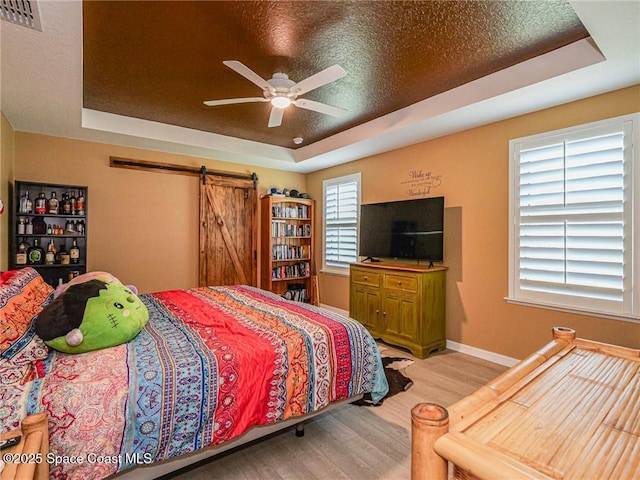 9025 106th Ave, Vero Beach, FL 32967 - bedroom with a tray ceiling, light wood finished floors, a barn door, and ceiling fan