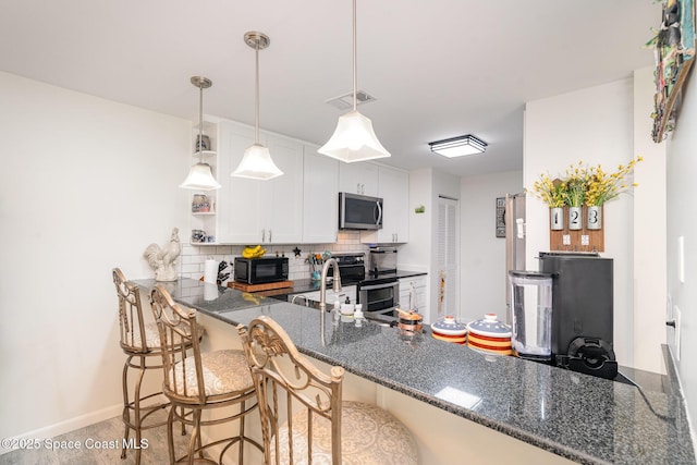 1100 SE Mitchell Ave Unit 204, Port St Lucie, FL 34952 - kitchen featuring appliances with stainless steel finishes, a peninsula, backsplash, white cabinetry, and dark stone countertops