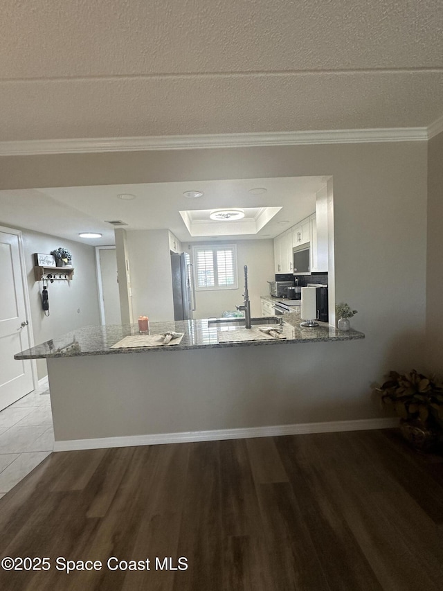 3210 N Harbor City Blvd Unit 316, Melbourne, FL 32935 - kitchen with appliances with stainless steel finishes, stone counters, wood finished floors, a peninsula, and a raised ceiling