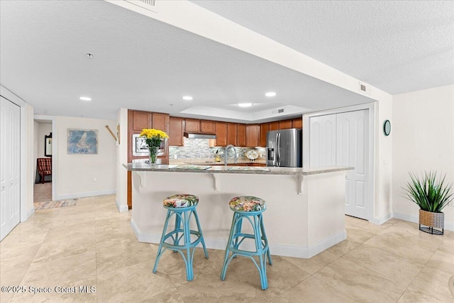 121 Lancha Cir Unit 203, Indian Harbour Beach, FL 32937 - kitchen featuring stainless steel refrigerator with ice dispenser, a textured ceiling, a kitchen bar, recessed lighting, and brown cabinetry