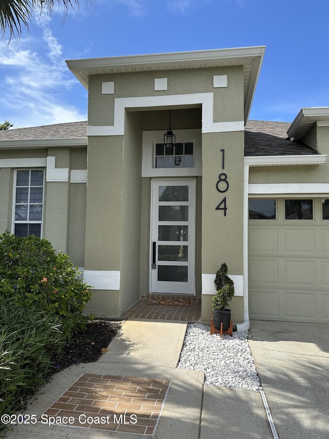 184 Calico Ln, Indialantic, FL 32903 - doorway to property with stucco siding, an attached garage, and a shingled roof
