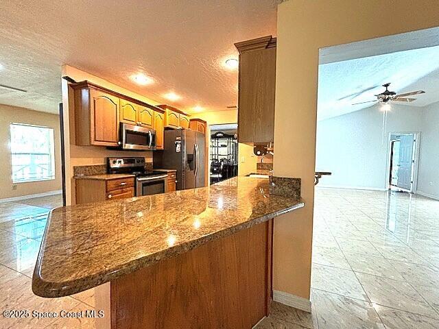 961 Haas Ave NE, Palm Bay, FL 32907 - kitchen featuring appliances with stainless steel finishes, a textured ceiling, dark stone counters, brown cabinetry, and a ceiling fan