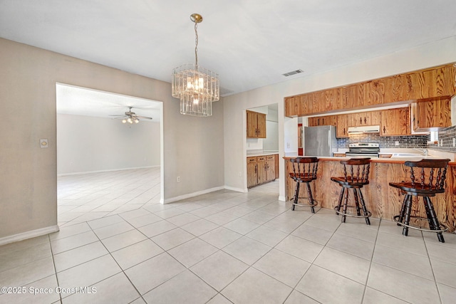 1081 Sunswept Rd NE, Palm Bay, FL 32905 - kitchen featuring stainless steel appliances, under cabinet range hood, brown cabinets, a chandelier, and open floor plan