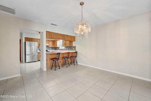 1081 Sunswept Rd NE, Palm Bay, FL 32905 - kitchen with freestanding refrigerator, brown cabinetry, a peninsula, decorative backsplash, and a chandelier
