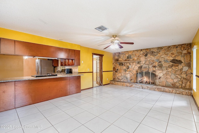 755 Haftez St NE, Palm Bay, FL 32907 - kitchen with freestanding refrigerator, a ceiling fan, a stone fireplace, light stone counters, and brown cabinets