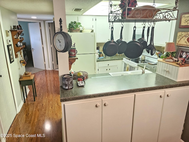 997 Sonesta Ave NE Unit 202, Palm Bay, FL 32905 - kitchen featuring freestanding refrigerator, wood finished floors, dark countertops, and white cabinets
