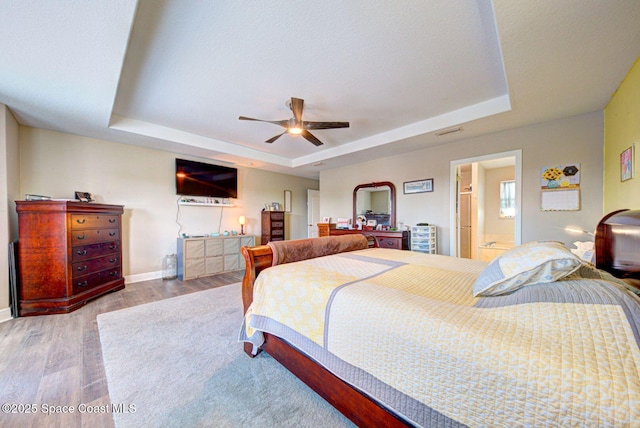 4082 Brantley Cir, Rockledge, FL 32955 - bedroom featuring a tray ceiling, wood finished floors, a ceiling fan, and connected bathroom