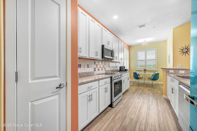 3930 Playa Del Sol Dr Unit 106, Rockledge, FL 32955 - kitchen with stainless steel appliances, light wood finished floors, decorative backsplash, white cabinets, and light stone countertops