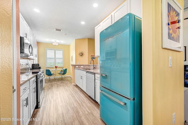3930 Playa Del Sol Dr Unit 106, Rockledge, FL 32955 - kitchen featuring appliances with stainless steel finishes, light wood-style floors, white cabinetry, light stone countertops, and a textured ceiling