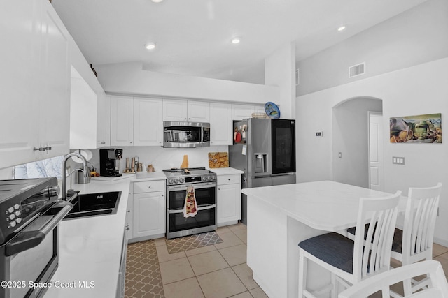 740 Indian Oaks Dr, Melbourne, FL 32901 - kitchen featuring appliances with stainless steel finishes, arched walkways, white cabinetry, light tile patterned floors, and vaulted ceiling