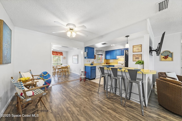 1242 Creel Rd NE, Palm Bay, FL 32905 - kitchen featuring blue cabinets, a textured ceiling, light countertops, a kitchen breakfast bar, and dark wood-style flooring