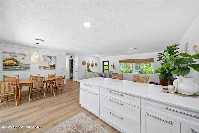 212 Ormond Dr, Indialantic, FL 32903 - kitchen featuring a textured ceiling, white cabinets, light wood-style flooring, light stone countertops, and decorative light fixtures