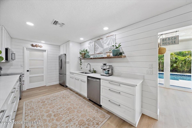 212 Ormond Dr, Indialantic, FL 32903 - kitchen featuring appliances with stainless steel finishes, white cabinetry, a textured ceiling, light wood-style floors, and wooden walls