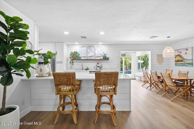 212 Ormond Dr, Indialantic, FL 32903 - kitchen featuring a textured ceiling, wood finished floors, light countertops, a breakfast bar, and white cabinetry