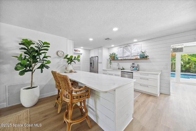 212 Ormond Dr, Indialantic, FL 32903 - kitchen featuring appliances with stainless steel finishes, light wood-style flooring, a peninsula, white cabinets, and a textured ceiling
