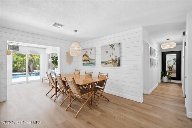 212 Ormond Dr, Indialantic, FL 32903 - dining space with light wood-style floors, a textured ceiling, and wood walls