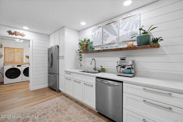 212 Ormond Dr, Indialantic, FL 32903 - kitchen with stainless steel appliances, separate washer and dryer, white cabinetry, light wood-style floors, and wooden walls