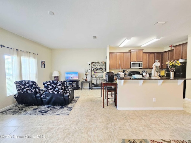 2735 Revolution St Unit 101, Melbourne, FL 32935 - kitchen with stainless steel microwave, a kitchen bar, dark countertops, refrigerator, and light tile patterned floors