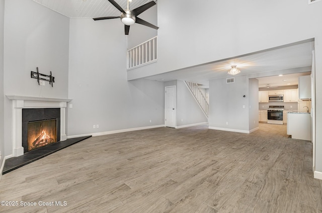 1250 Admiralty Blvd, Rockledge, FL 32955 - unfurnished living room featuring a lit fireplace, a ceiling fan, a towering ceiling, light wood-style flooring, and stairs