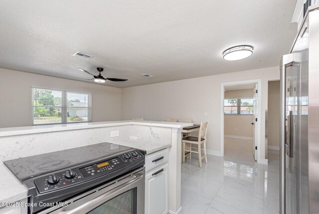 1245 Arlington Cir, Merritt Island, FL 32952 - kitchen with stainless steel appliances, a ceiling fan, healthy amount of natural light, white cabinets, and a textured ceiling