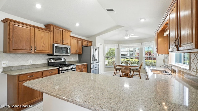 7927 Citrus Creek Dr, Melbourne, FL 32940 - kitchen featuring stainless steel appliances, brown cabinetry, a ceiling fan, decorative backsplash, and a peninsula