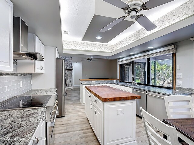 3090 Rio Pino S, Indialantic, FL 32903 - kitchen with wooden counters, a ceiling fan, a raised ceiling, appliances with stainless steel finishes, and wall chimney range hood