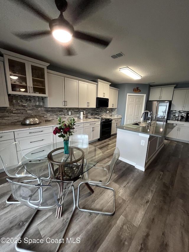 1015 Swiss Pointe Ln, Rockledge, FL 32955 - kitchen featuring black appliances, backsplash, ceiling fan, dark wood-type flooring, and a kitchen island with sink