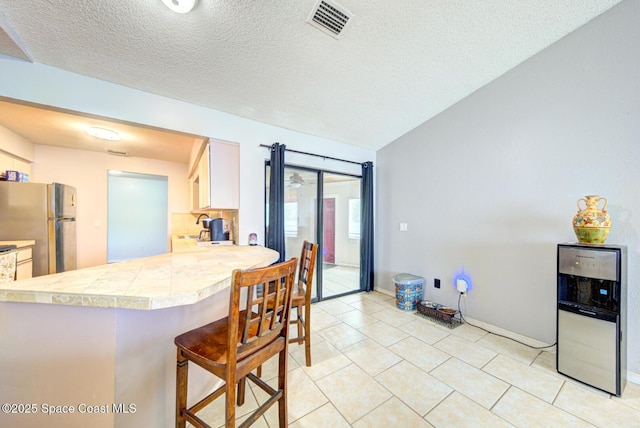 2169 Wagonwheel Ave SE, Palm Bay, FL 32909 - kitchen with freestanding refrigerator, a kitchen bar, light tile patterned flooring, a textured ceiling, and a peninsula