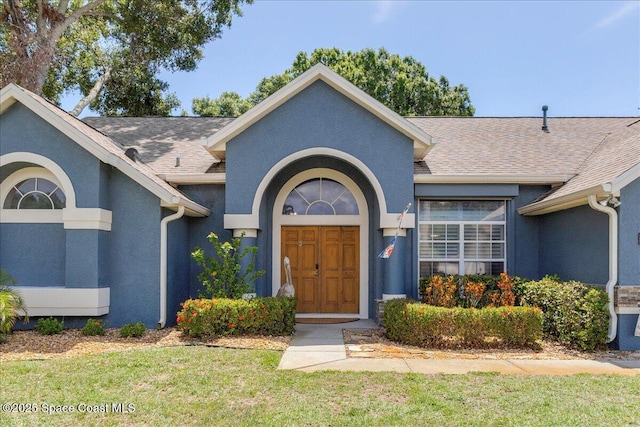 970 Pelican Ln, Rockledge, FL 32955 - doorway to property featuring stucco siding, roof with shingles, and a yard