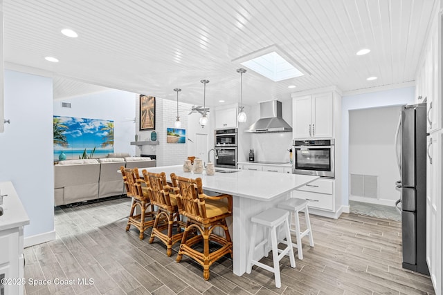2945 Newfound Harbor Dr, Merritt Island, FL 32952 - kitchen featuring wall chimney range hood, a skylight, stainless steel appliances, a kitchen bar, and light countertops