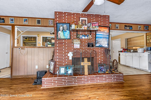 1714 Blanche Ave, Melbourne, FL 32934 - living room with a textured ceiling, wood finished floors, ceiling fan, a brick fireplace, and wood walls