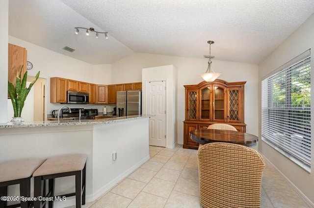 793 Ontario St NW, Palm Bay, FL 32907 - kitchen with stainless steel fridge with ice dispenser, lofted ceiling, a peninsula, light tile patterned floors, and light stone countertops