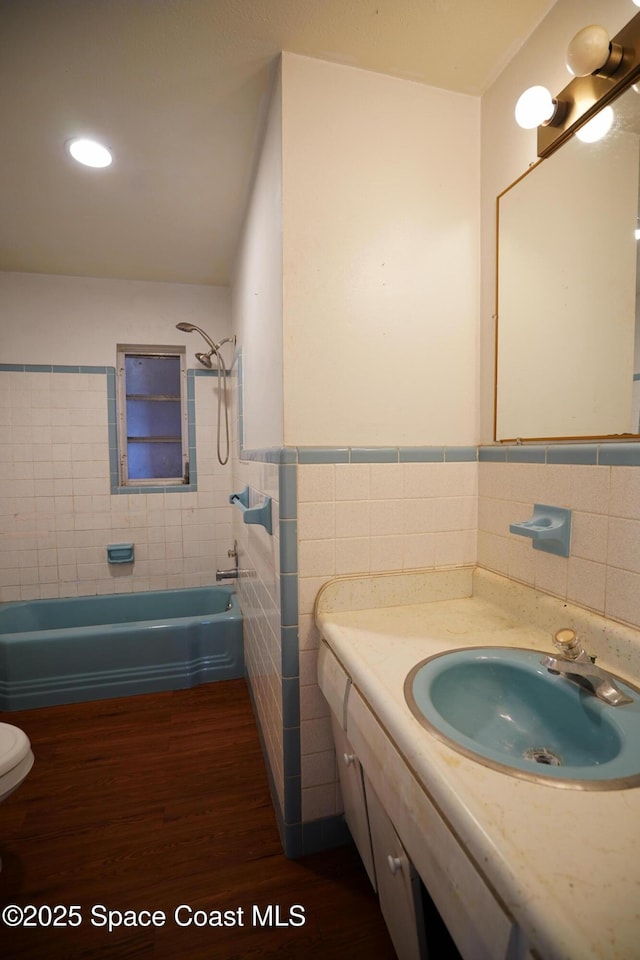 614 W Ct, Titusville, FL 32796 - bathroom featuring tile walls, wood finished floors, vanity, tub / shower combination, and a wainscoted wall