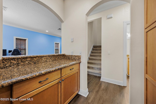 1375 Isabella Dr Unit 108, Melbourne, FL 32935 - kitchen with dark wood-type flooring, dark stone counters, arched walkways, recessed lighting, and brown cabinetry