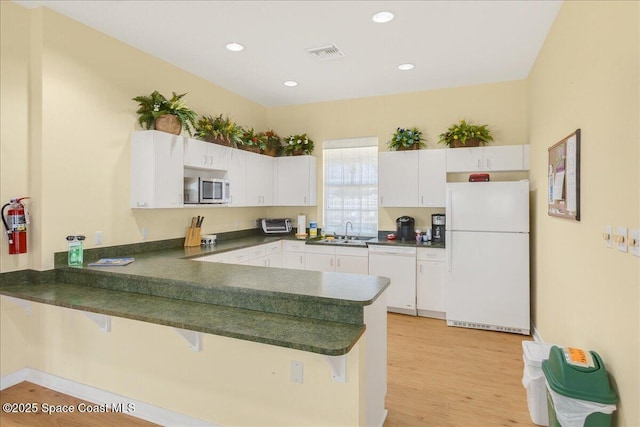608 Lorelei Ave, Melbourne, FL 32901 - kitchen with white appliances, dark countertops, a peninsula, white cabinets, and a kitchen breakfast bar