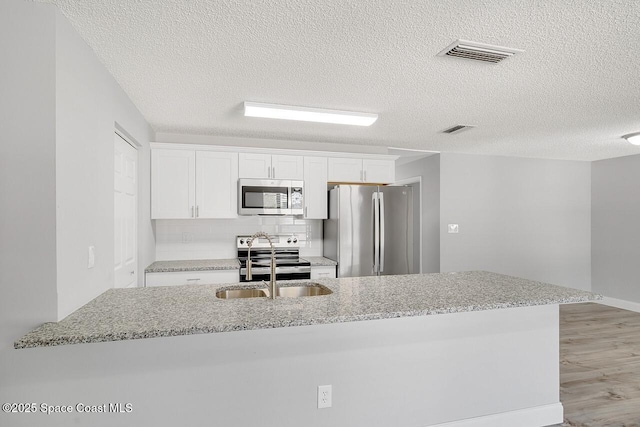 1256 16th Ave SW, Vero Beach, FL 32962 - kitchen with appliances with stainless steel finishes, white cabinetry, light wood-style flooring, a textured ceiling, and light stone counters