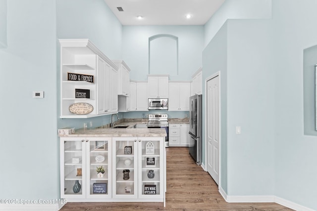 2690 Camberly Cir, Melbourne, FL 32940 - kitchen featuring appliances with stainless steel finishes, white cabinets, a peninsula, light wood-style floors, and a high ceiling