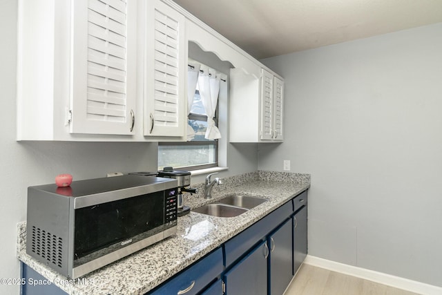 583 Mandan Ave, Melbourne, FL 32935 - kitchen featuring stainless steel microwave, blue cabinetry, light wood finished floors, and white cabinetry