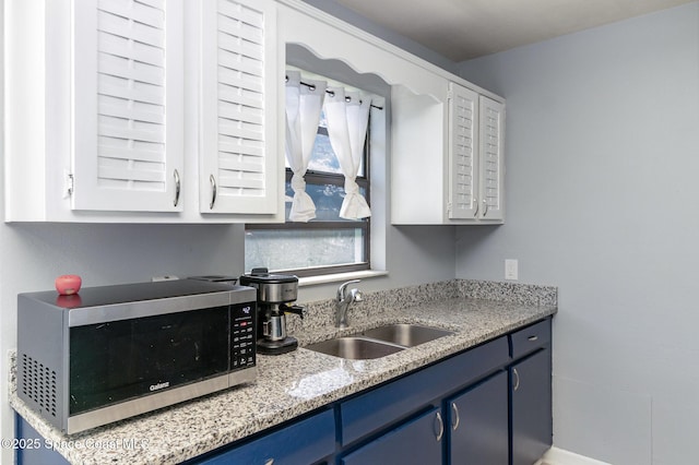 583 Mandan Ave, Melbourne, FL 32935 - kitchen featuring stainless steel microwave, blue cabinetry, white cabinets, and light stone counters