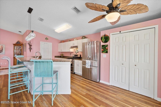 2627 Deercroft Dr, Melbourne, FL 32940 - kitchen with stainless steel appliances, lofted ceiling, white cabinets, under cabinet range hood, and light wood finished floors