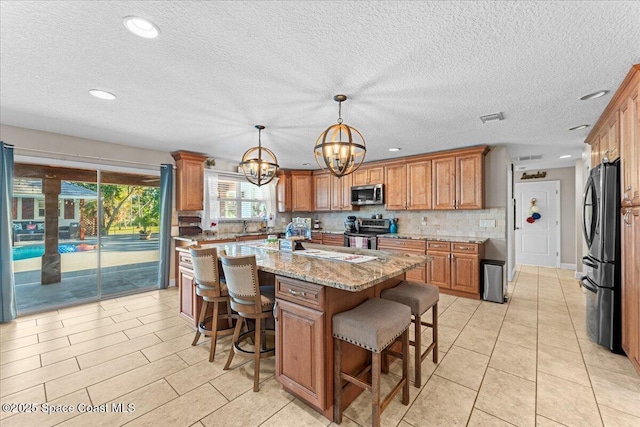 260 Utopia Cir, Merritt Island, FL 32952 - kitchen featuring appliances with stainless steel finishes, a chandelier, brown cabinetry, light stone countertops, and a breakfast bar