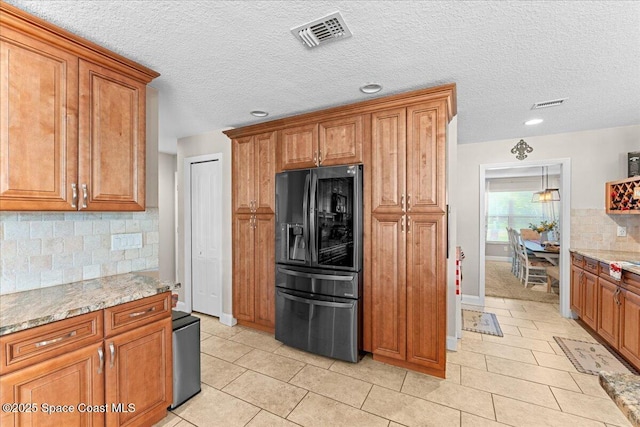 260 Utopia Cir, Merritt Island, FL 32952 - kitchen featuring refrigerator with ice dispenser, brown cabinets, tasteful backsplash, light tile patterned floors, and light stone counters