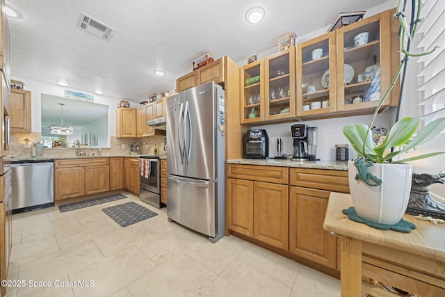 743 Palm Springs Cir, Satellite Beach, FL 32937 - kitchen with appliances with stainless steel finishes, under cabinet range hood, glass insert cabinets, decorative backsplash, and brown cabinetry