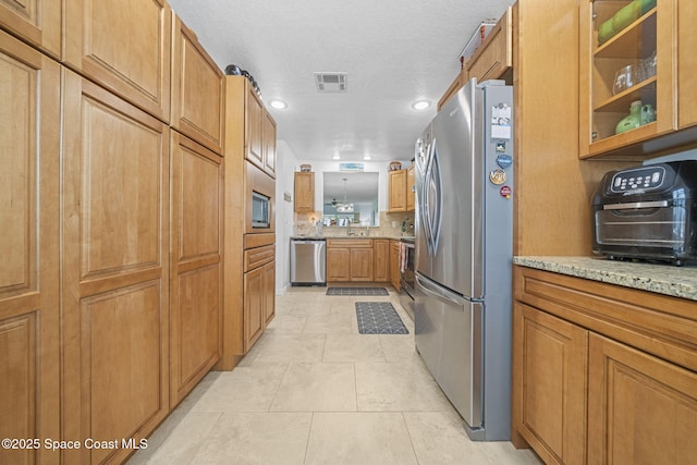 743 Palm Springs Cir, Satellite Beach, FL 32937 - kitchen featuring appliances with stainless steel finishes, brown cabinets, recessed lighting, light stone counters, and a textured ceiling