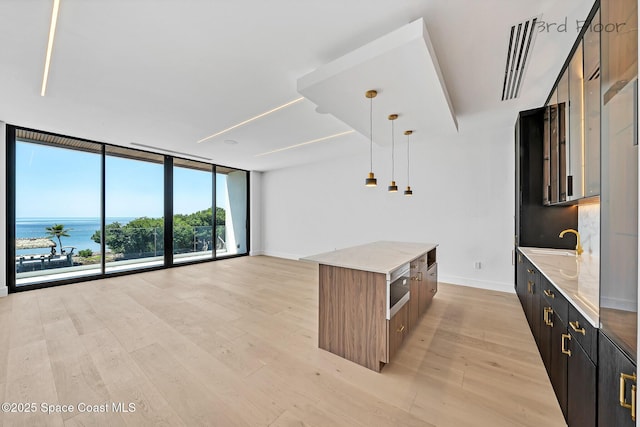 16 Seaside Ave, Key Largo, FL 33037 - kitchen featuring a wall of windows, a center island, light wood-type flooring, light stone counters, and hanging light fixtures