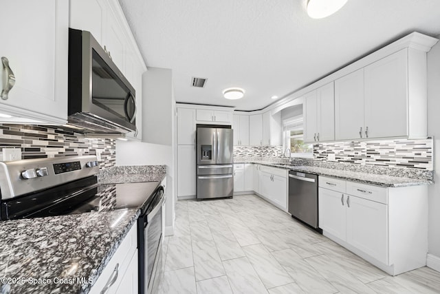 959 Macco Rd, Cocoa, FL 32927 - kitchen featuring stainless steel appliances, light marble finish flooring, decorative backsplash, dark stone countertops, and white cabinetry